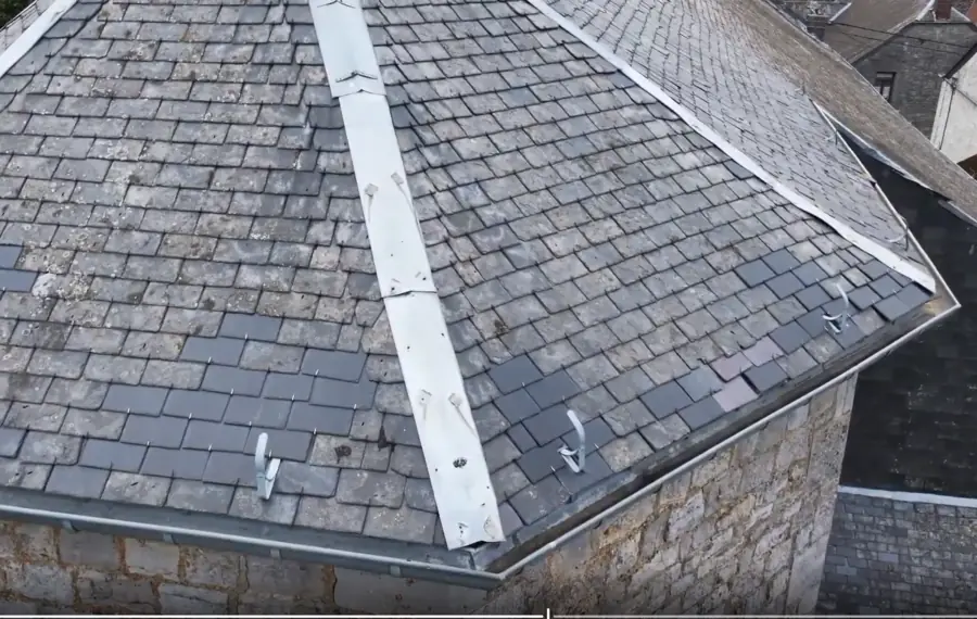 Croupe d'une toiture d'ardoises : deux arêtiers en zinc convergent vers le faîte, crochets de sécurité fixés sur les rangs.