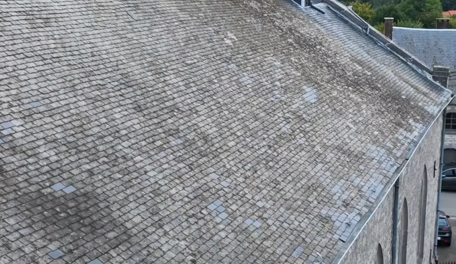 Toiture d'une nef d'église en ardoises, vue en enfilade depuis le faîte jusqu'au chevet ; les ardoises remplacées apparaissent plus claires que les anciennes.