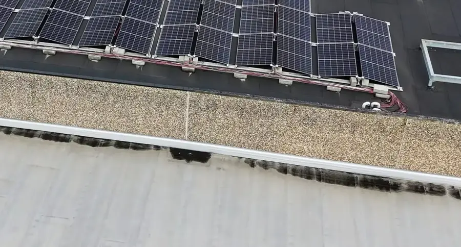 Bord d'une toiture plate : la dernière rangée de modules s'arrête à quelques dizaines de centimètres de l'acrotère en béton, un faisceau de câbles rouges et noirs court à même la membrane le long des supports.