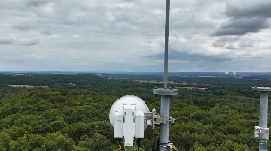 Sommet d'un pylône de télécommunication portant des antennes et une parabole, au-dessus d'une forêt s'étendant jusqu'à l'horizon.