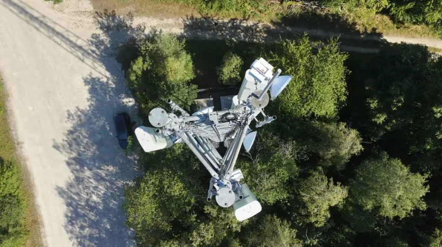 Pylône vu à la verticale depuis le dessus : les bras supportant les antennes forment une étoile au-dessus du chemin d'accès et des arbres.