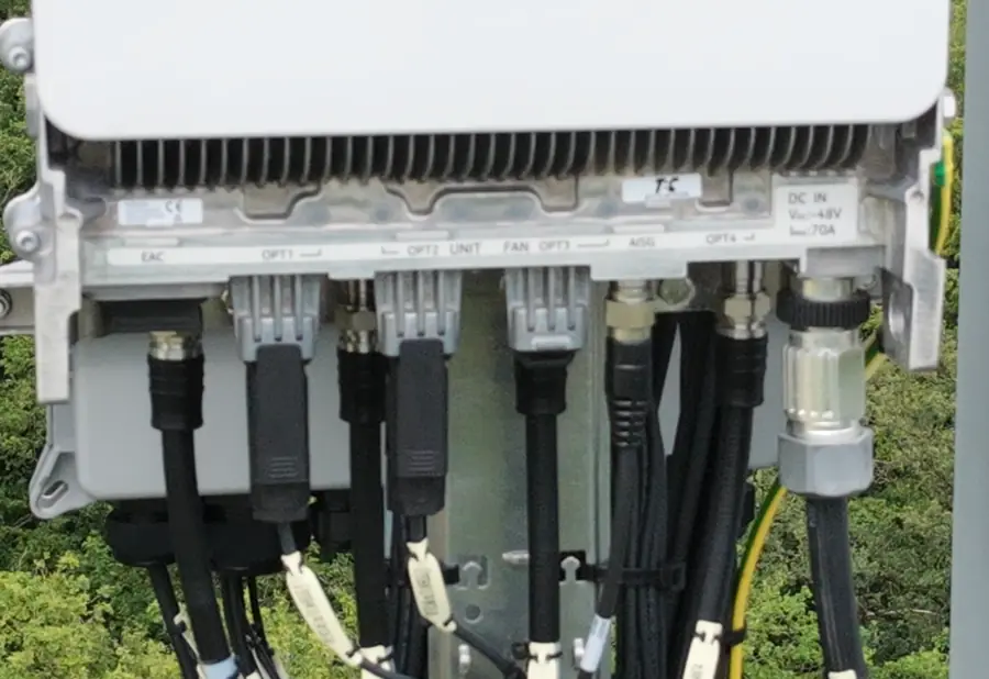 Dessous d'un équipement radio monté en haut de pylône : sérigraphie des ports EAC, OPT1 à OPT4, ALIM et DC IN, connecteurs optiques et câbles repérés par des étiquettes.