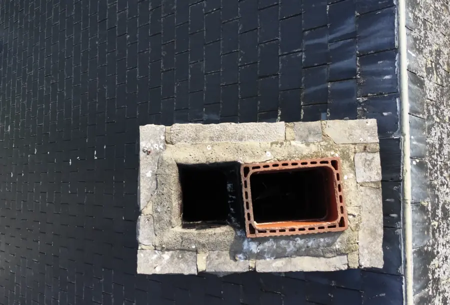 Vue verticale du couronnement d'une souche de cheminée en pierre : deux conduits, celui de droite chemisé d'un boisseau en terre cuite, celui de gauche à nu. Ardoises et solin plomb tout autour.