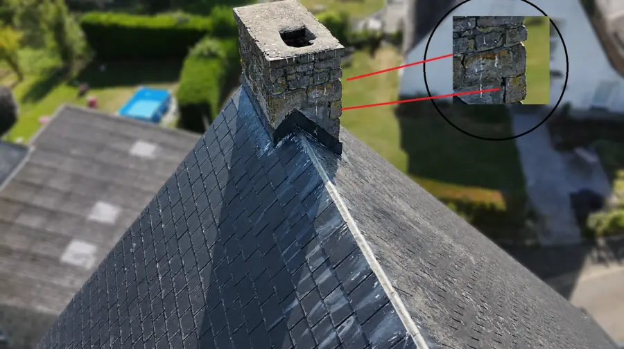 Souche de cheminée en pierre au sommet d'un versant d'ardoises ; deux traits rouges relient une face de la souche à un agrandissement circulaire montrant des joints creusés et des pierres déchaussées.
