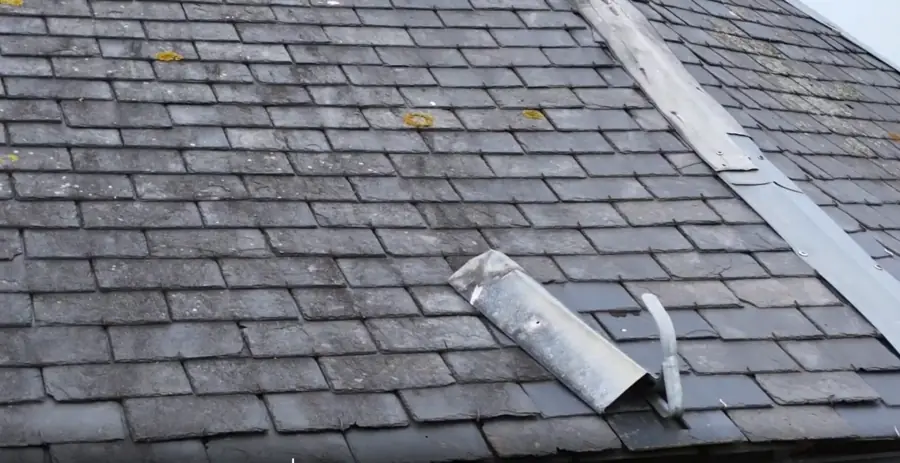 Pièce de zinc cylindrique descellée, posée en travers des ardoises d'un versant, gouttière et arête visibles.